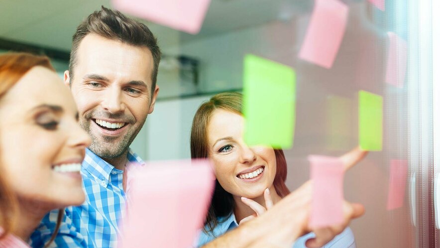 Drei Personen vor einer Glasscheibe mit Klebezetteln Drei Personen, ein Mann und zwei Frauen, vor einer mit Klebezetteln versehenen Glasscheibe.