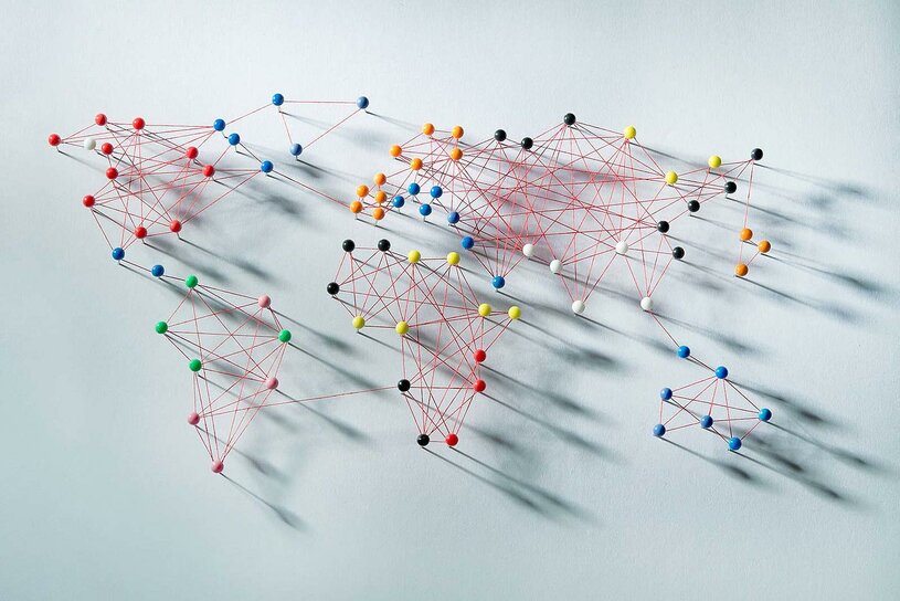 Darstellung einer globalen Kommunikation anhand miteinander verbundener Stecknadeln, die eine Weltkarte ergeben.
